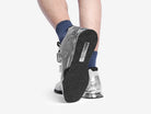 A person showing the underside of the silver weightlifting shoes on a white background