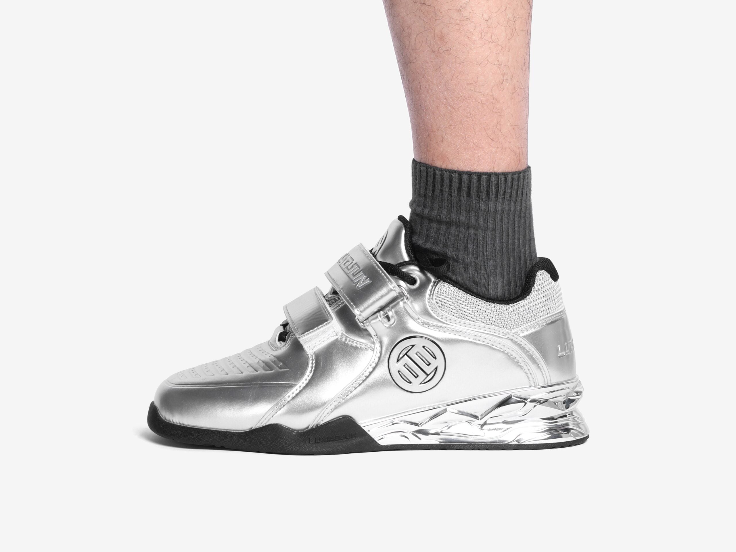A person wearing the silver weightlifting shoes showing the outer side that shows the logo of luxiaojun