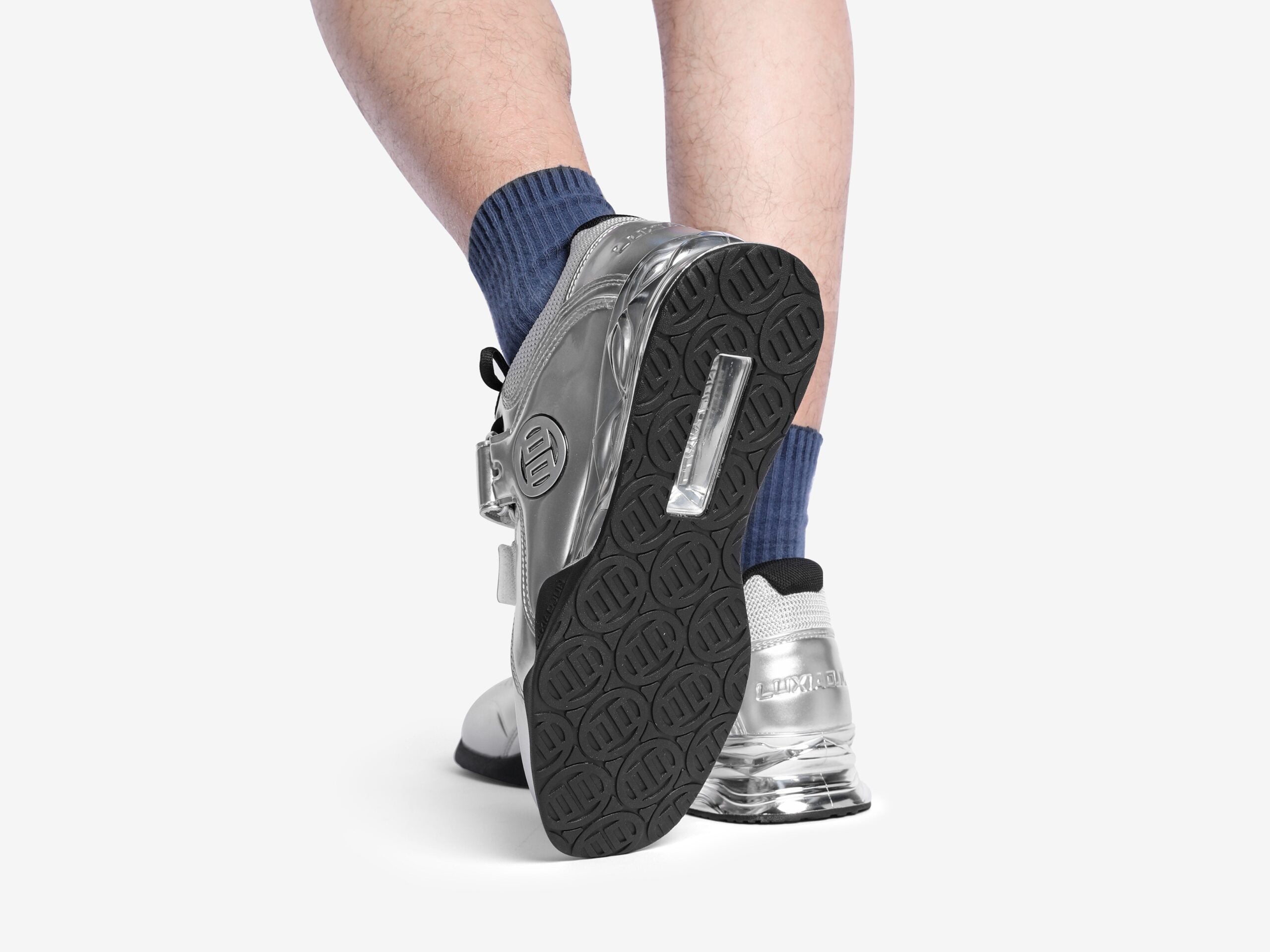 A person showing the underside of the silver weightlifting shoes on a white background