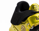 Close-up of a yellow gold and black shoe with a brand logo on a white background