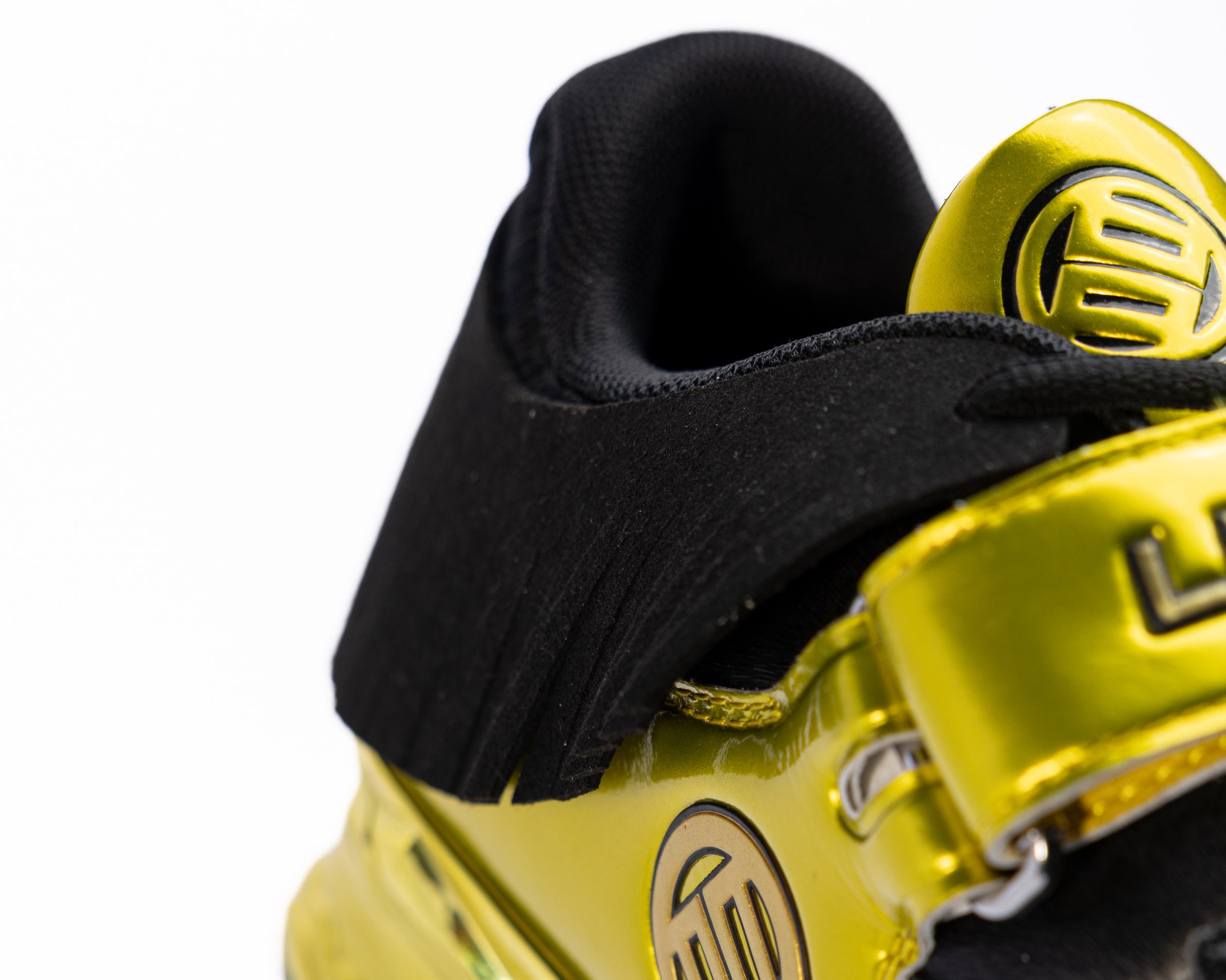 Close-up of a yellow gold and black shoe with a brand logo on a white background